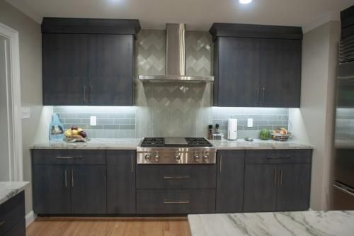 Modern kitchen with dark blue cabinets, stainless steel appliances, and gray tiled backsplash. Counter lighting illuminates the countertop.