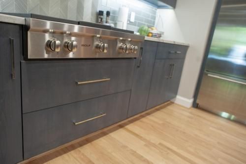 Grey kitchen cabinets with a stainless steel stove and light wood floors. A stainless steel refrigerator is partially visible on the right.