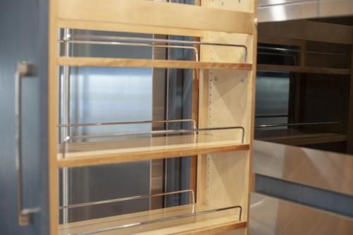 A pull-out spice rack installed in a kitchen cabinet. It has three shelves with chrome railings.