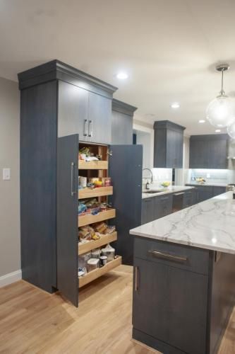 Tall blue kitchen pantry with pull-out shelves open, revealing food items. A kitchen island and additional cabinets are also visible.