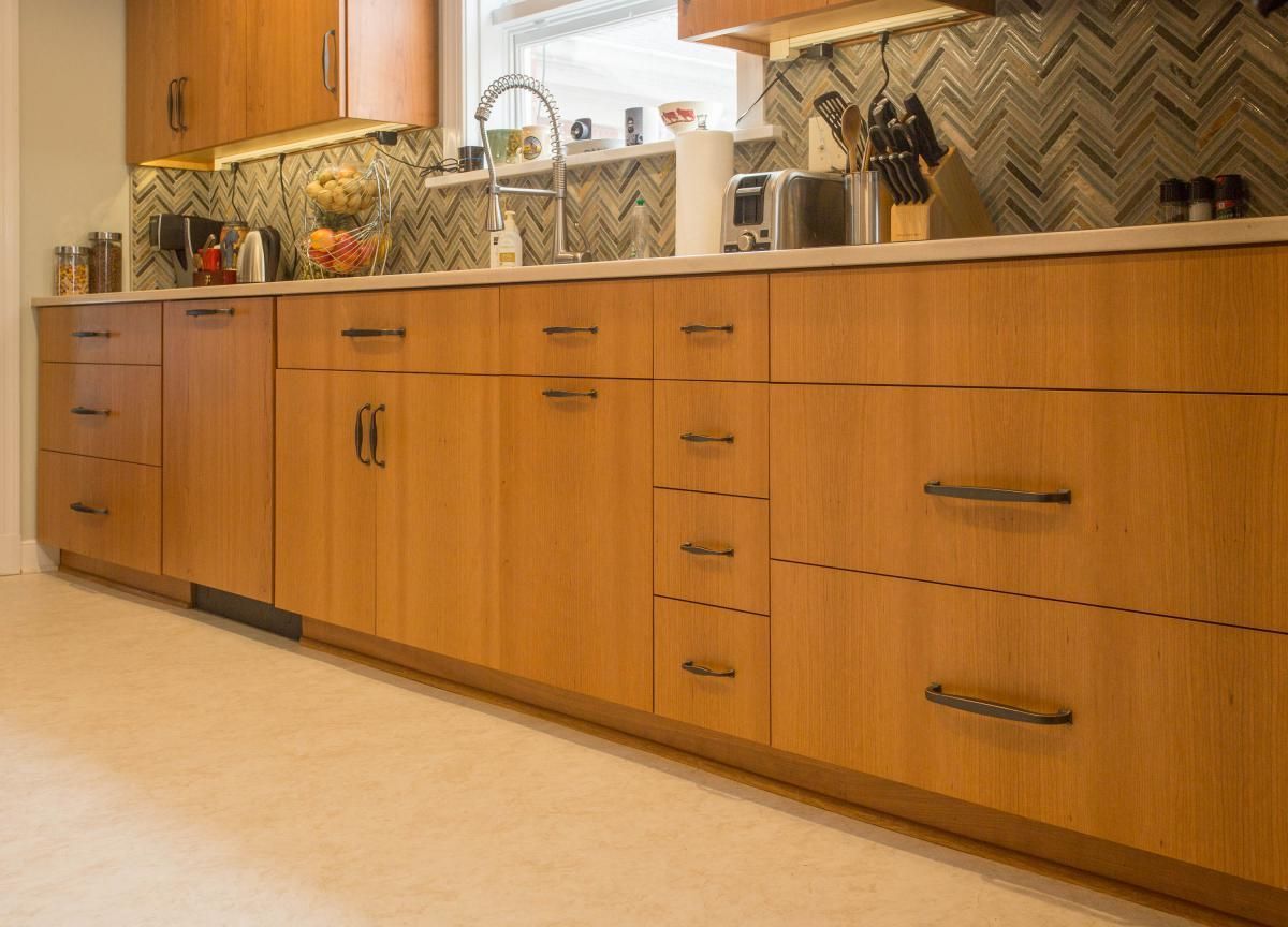Light wood kitchen cabinets with dark hardware and a light countertop, along with a backsplash and sink.