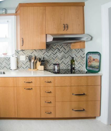 Light wood kitchen with a patterned backsplash, stainless steel range hood, and a small window.
