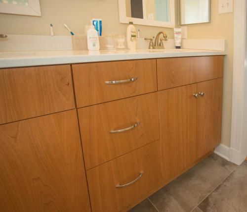 Bathroom vanity with wooden cabinets, silver handles, and a white countertop. The bathroom has tile floors.