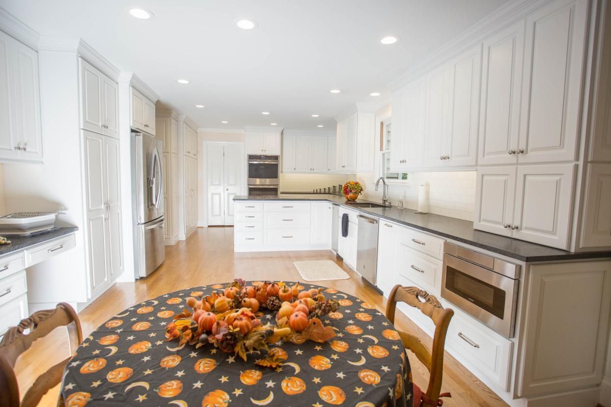 A bright white kitchen with hardwood floors, a round table set for Halloween with a fall wreath, and stainless steel appliances.