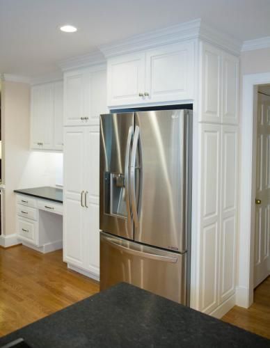 A stainless steel refrigerator built into white kitchen cabinets with a desk and a black countertop.