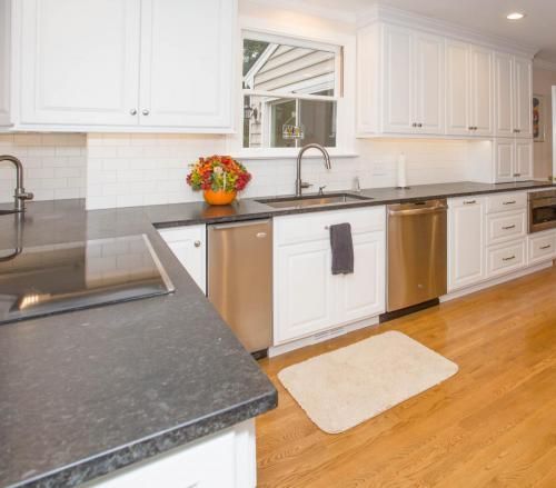 White kitchen with stainless steel appliances, black countertops, and a window above the sink.