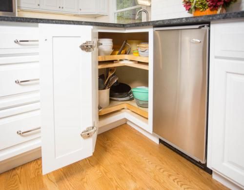 A white kitchen cabinet corner with a pull-out lazy susan holding dishes, and a stainless steel wine fridge.