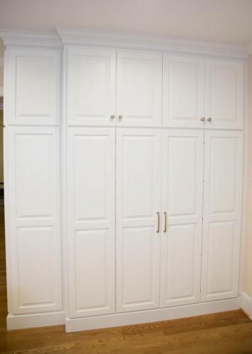 Tall, white built-in cabinets against a wall. The cabinets have raised panel doors, silver hardware, and are topped with molding.