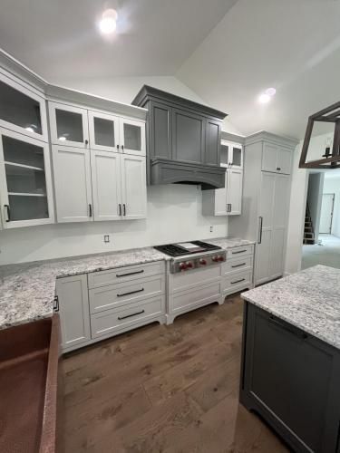 Modern kitchen with white cabinets, gray range hood, granite countertops, and wood floors.