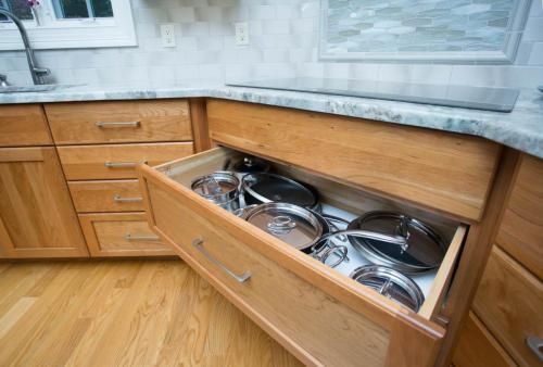 Wooden kitchen cabinet drawer open, filled with pots and pans. The drawer is under a countertop.