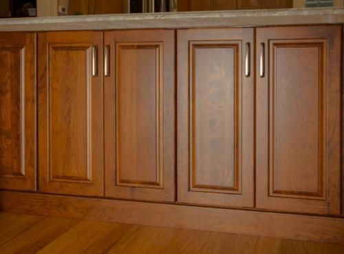 Wooden kitchen cabinets with brushed silver handles and a light-colored countertop. The cabinets are brown, and the floor is a lighter wood.