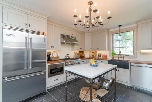 A well-lit kitchen with light gray cabinets, stainless steel appliances, a black tile floor, and a marble-topped island.