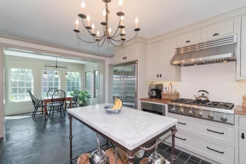Elegant kitchen with a marble-topped island and stainless steel appliances. View into a sunroom with a dining table.