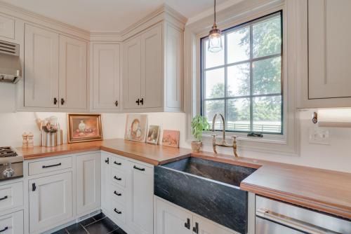 Kitchen corner with white cabinets, copper countertops, a black farmhouse sink, and a window with a view.