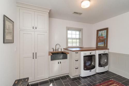 Laundry room with white cabinets, a black sink, and dark tiled floor. Washer and dryer sit beneath a wood countertop.