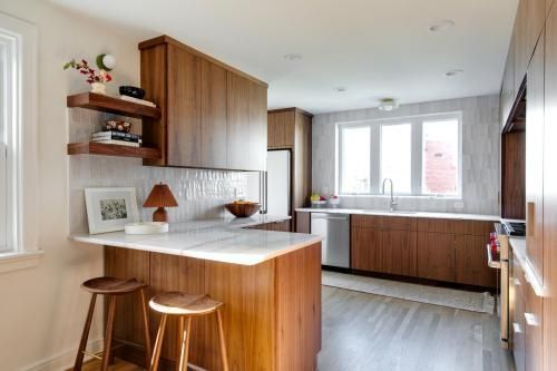 A modern kitchen with wood cabinets, a breakfast bar, and a white tile backsplash. Two wooden stools sit at the bar.