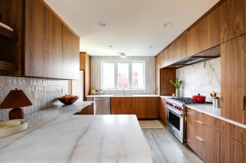 Modern kitchen with wood cabinets, marble countertops, and stainless steel appliances. A large window provides natural light.
