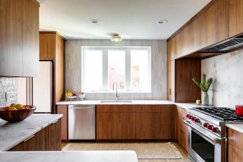 Modern kitchen with wood cabinets, stainless steel appliances, marble countertops, and a window above the sink.