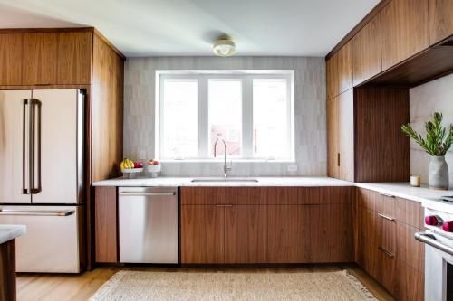 Modern kitchen with wooden cabinets, stainless steel appliances, and a white countertop. A window with natural light brightens the space.