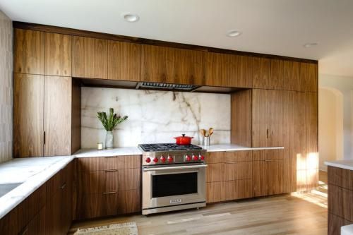Modern kitchen with walnut cabinets, a stainless steel range, and a marble backsplash. Natural light streams in.