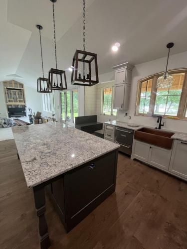 Spacious kitchen with a dark island and granite countertop, overhead pendant lights, and a copper sink.