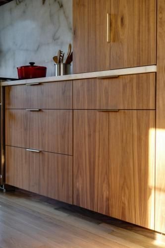 Wooden kitchen cabinets with horizontal wood grain and silver drawer pulls; a red pot and utensils are on the countertop.