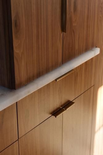 Wooden kitchen cabinets with brass handles and a marble countertop, illuminated by sunlight.