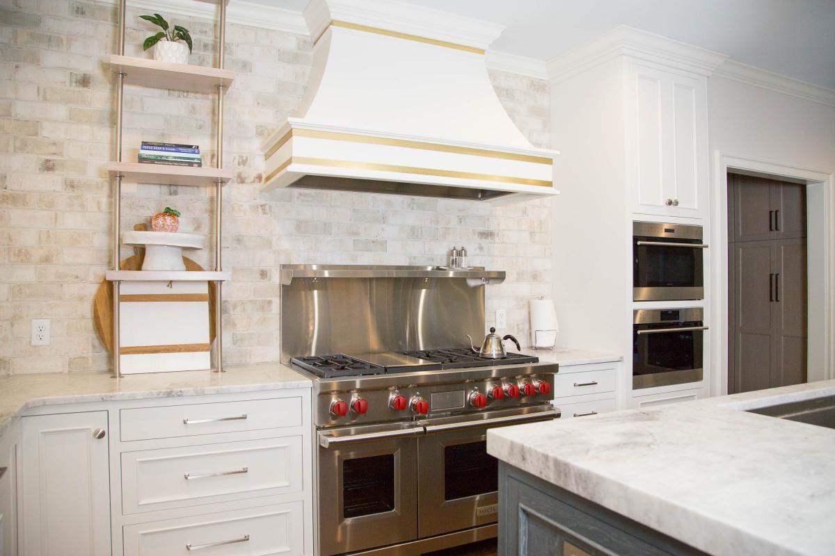 Kitchen with stainless steel range, white hood, and marble countertops against a brick backsplash.