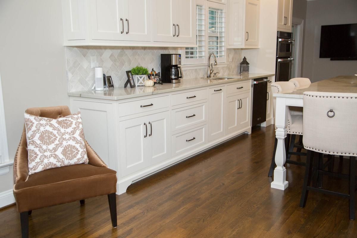 Kitchen with white cabinets, granite countertops, and dark wood floors; a brown armchair with a patterned pillow sits in the foreground.