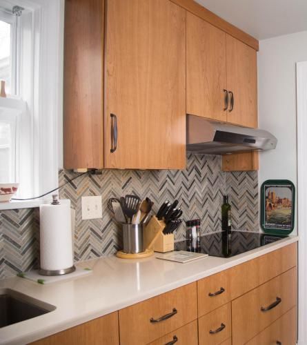 A kitchen with light wood cabinets, white countertops, and a backsplash of gray and white chevron tiles.
