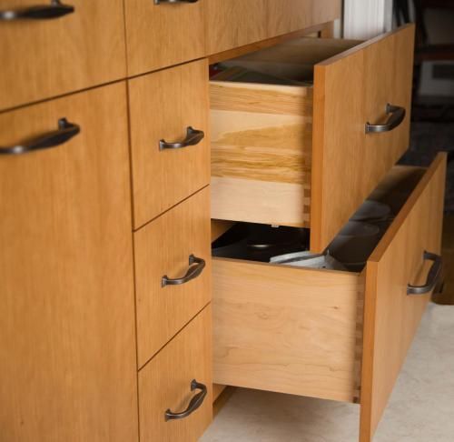 Wooden drawers partially opened, revealing contents and construction, with dark handles against light wood.