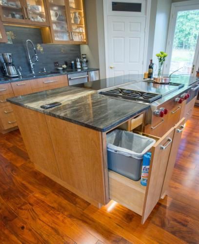 A modern kitchen island with a pull-out trash bin. The island has a granite countertop and a stovetop.