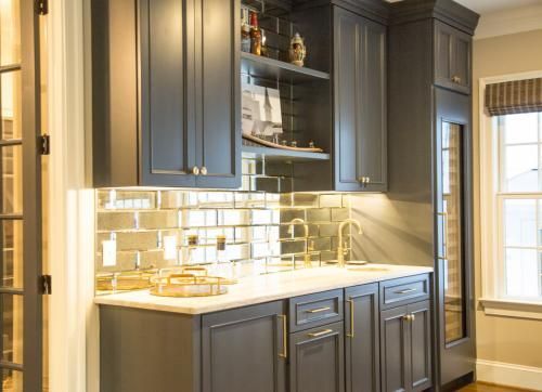 Dark gray home bar with mirrored backsplash, marble countertop, and gold fixtures. The bar has built-in cabinets and a wine fridge.