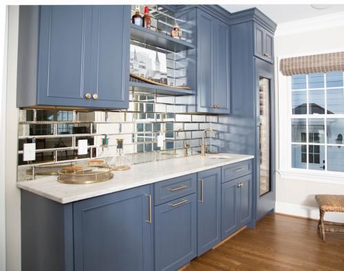 Blue built-in home bar with mirrored backsplash, white countertop, and a wine fridge.  A small window is to the right.