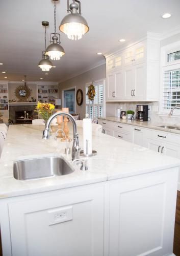 Bright, white kitchen with a large island, pendant lights, and cabinets. A stainless steel sink and faucet are in the island.