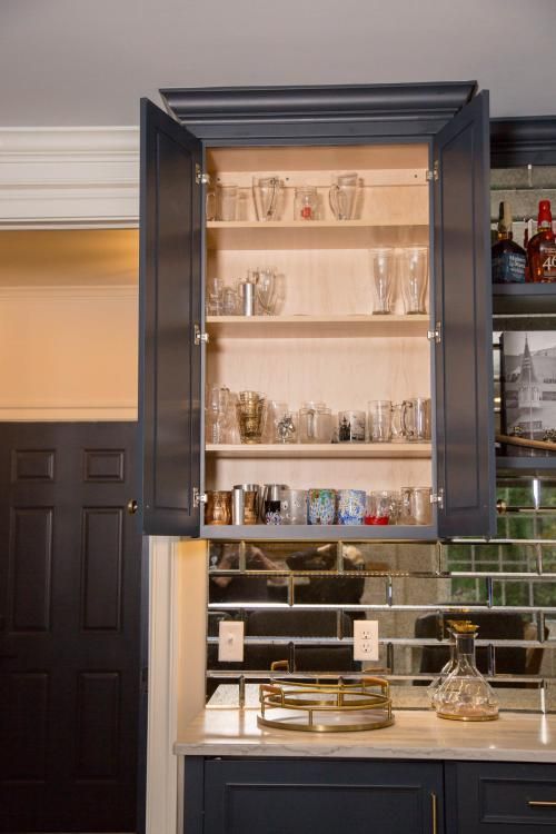 Dark blue upper cabinet with open doors showcasing glassware collection against mirrored backsplash.