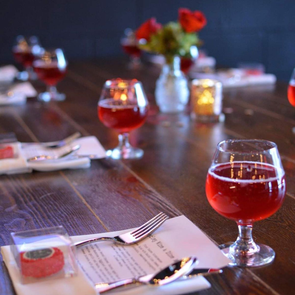 Table set with red wine glasses, silverware, and small red candies. Roses and candles in the background.