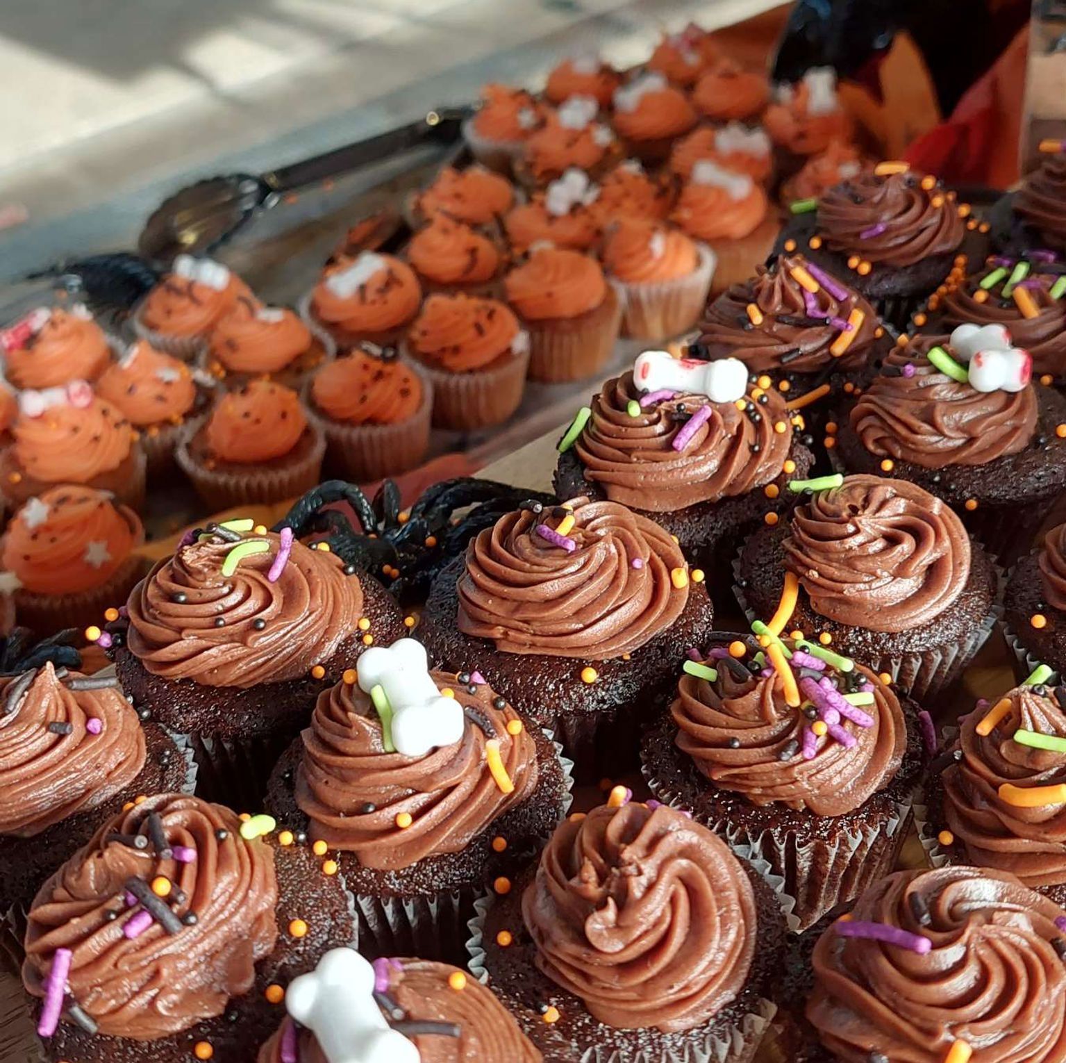 Halloween cupcakes with chocolate frosting and orange icing, decorated with sprinkles and bone-shaped candies.
