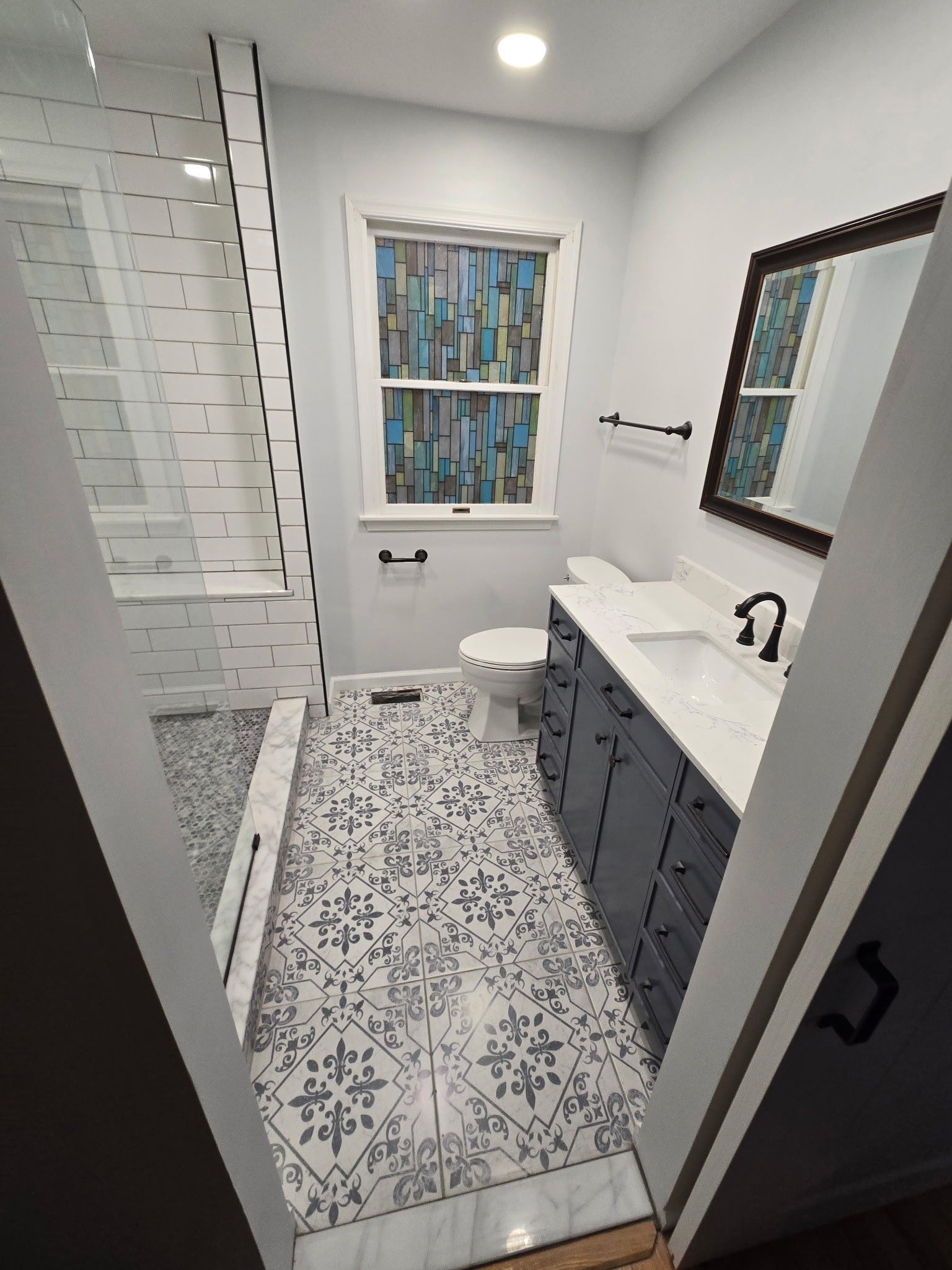 Bathroom with patterned floor tiles, blue vanity, and a glass shower.