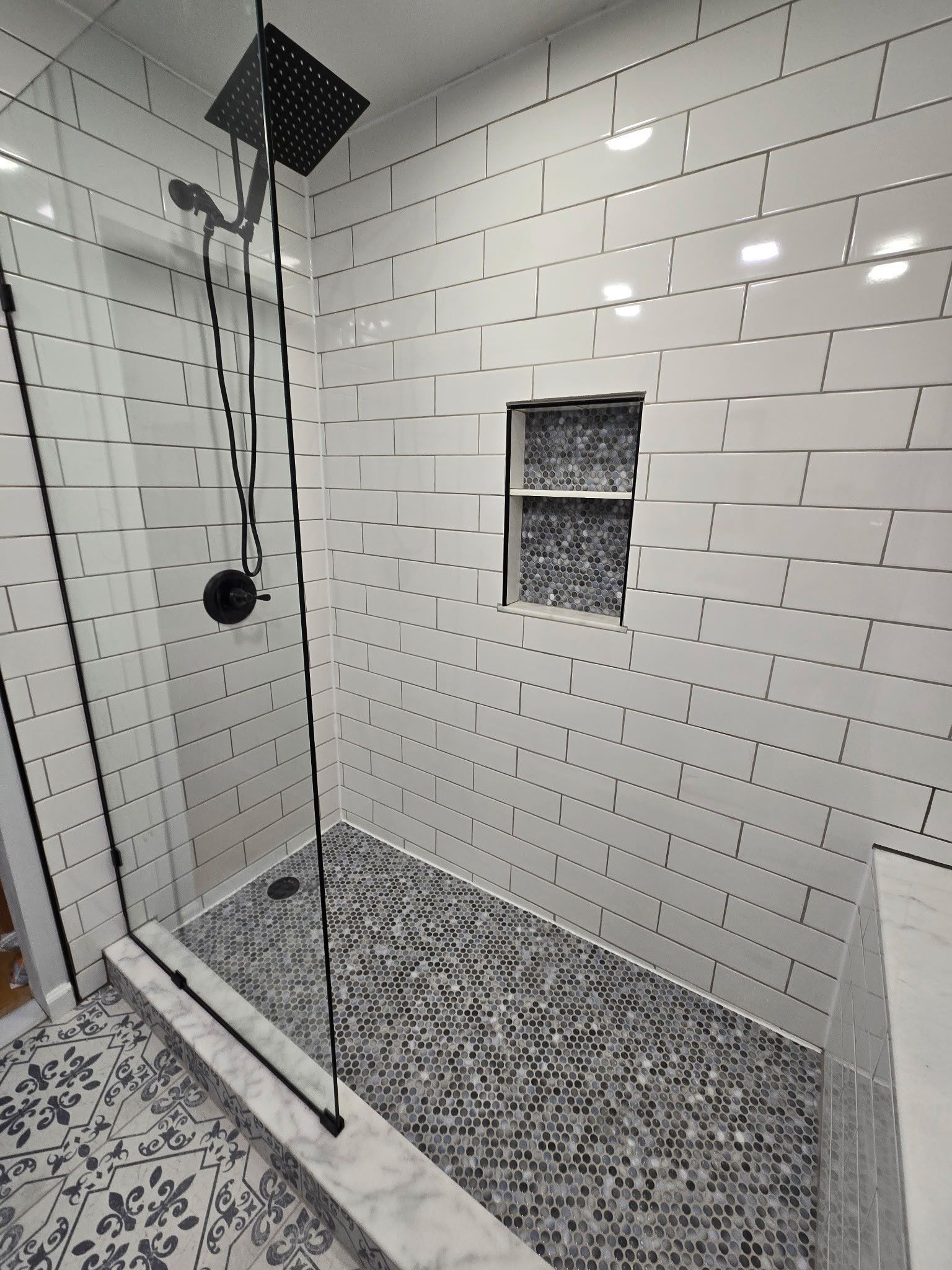 Modern bathroom with white subway tile walls, mosaic tile floor, glass shower door, and black fixtures.