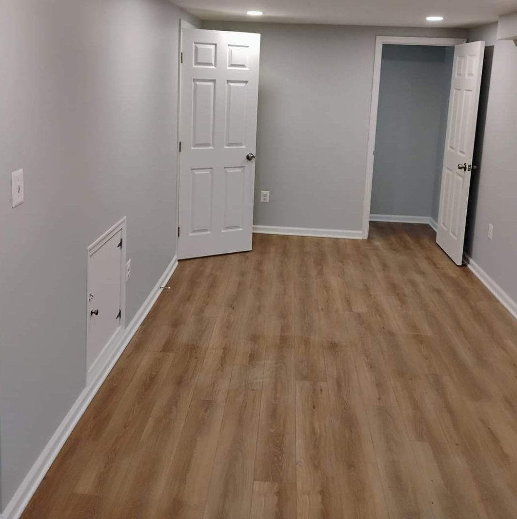 Empty room with wood-look flooring, gray walls, white doors, and ceiling lights.