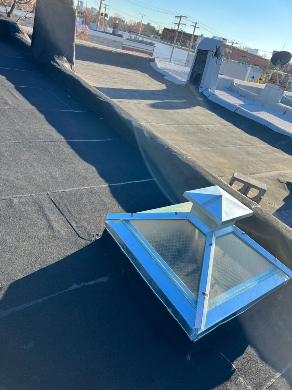 Black tar roof with a skylight, other roof structures, and city view.