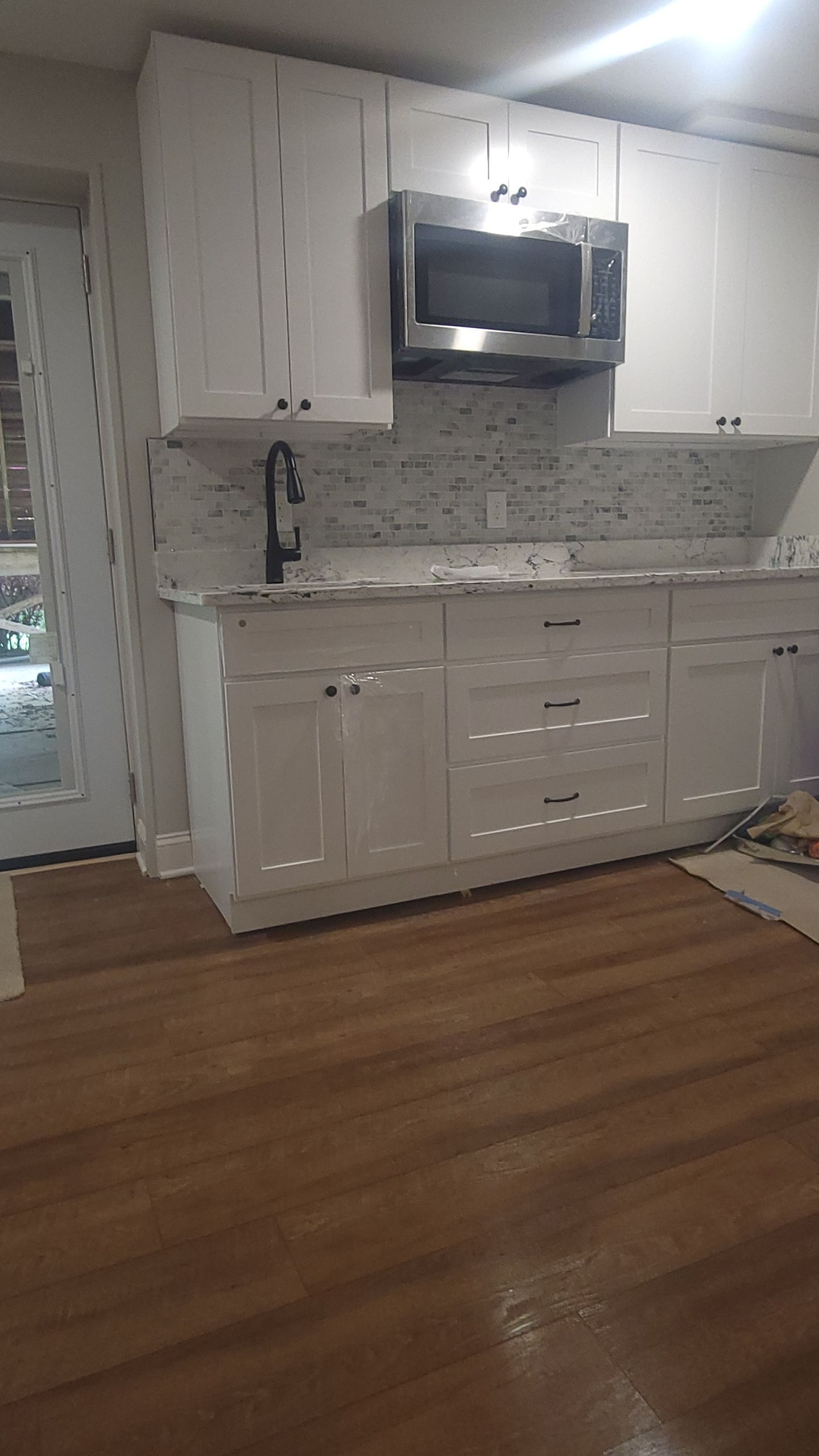White kitchen cabinets with a microwave, backsplash, and wooden floors.