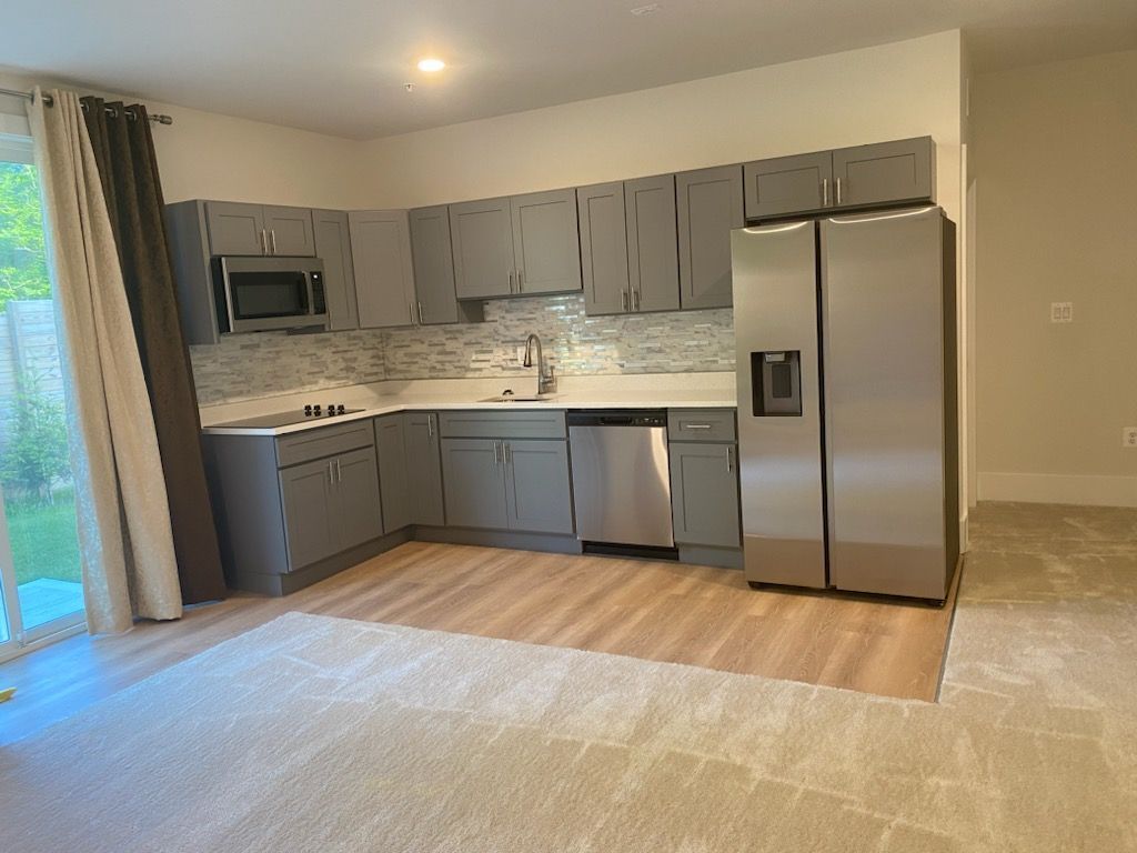 Gray kitchen with stainless steel appliances, light wood-look flooring, and a sliding glass door.