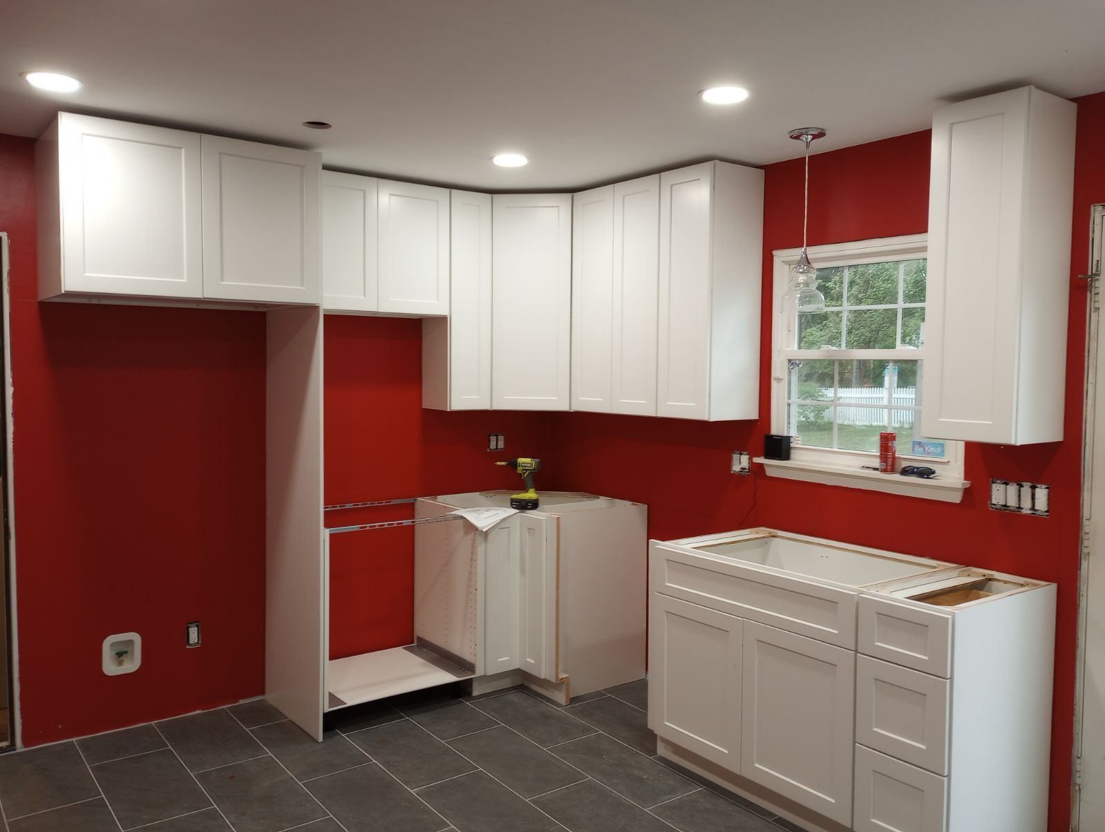 White kitchen cabinets installed against a red wall. Unfinished kitchen renovation.