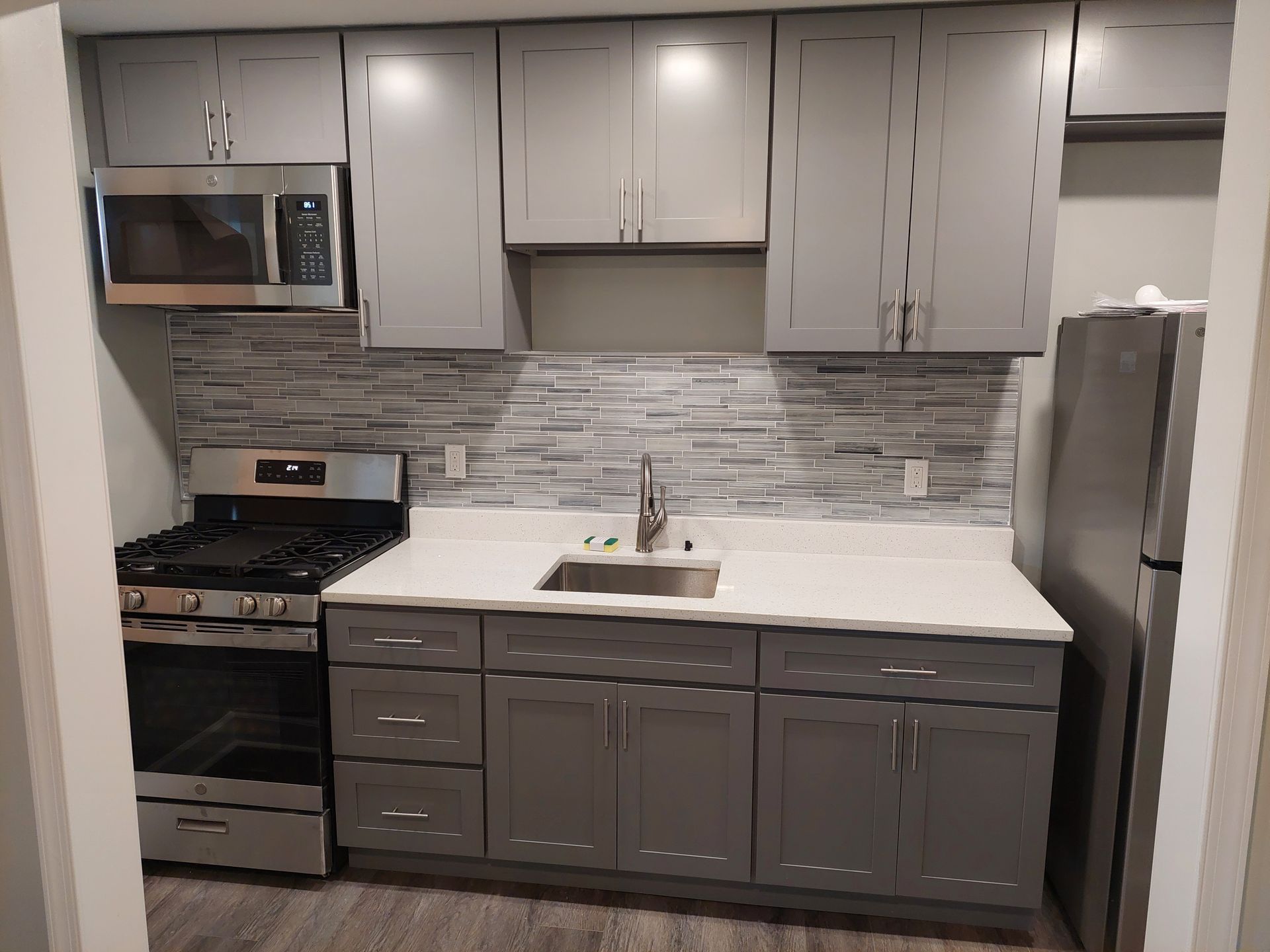 Gray kitchen cabinets, white countertop, stainless steel appliances, gray backsplash.