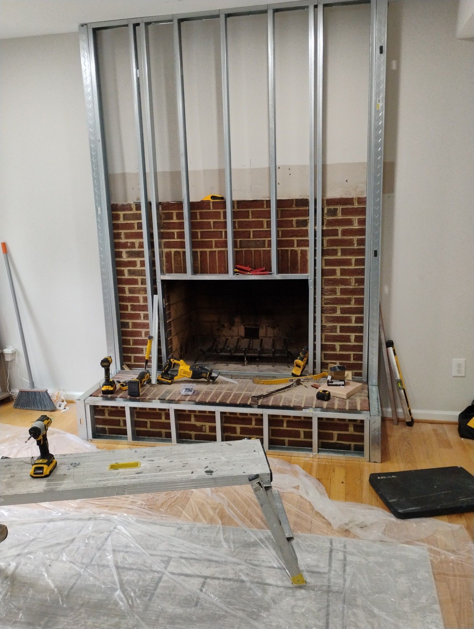 Metal stud framing installed around a brick fireplace. Construction tools and a work surface are in the foreground.