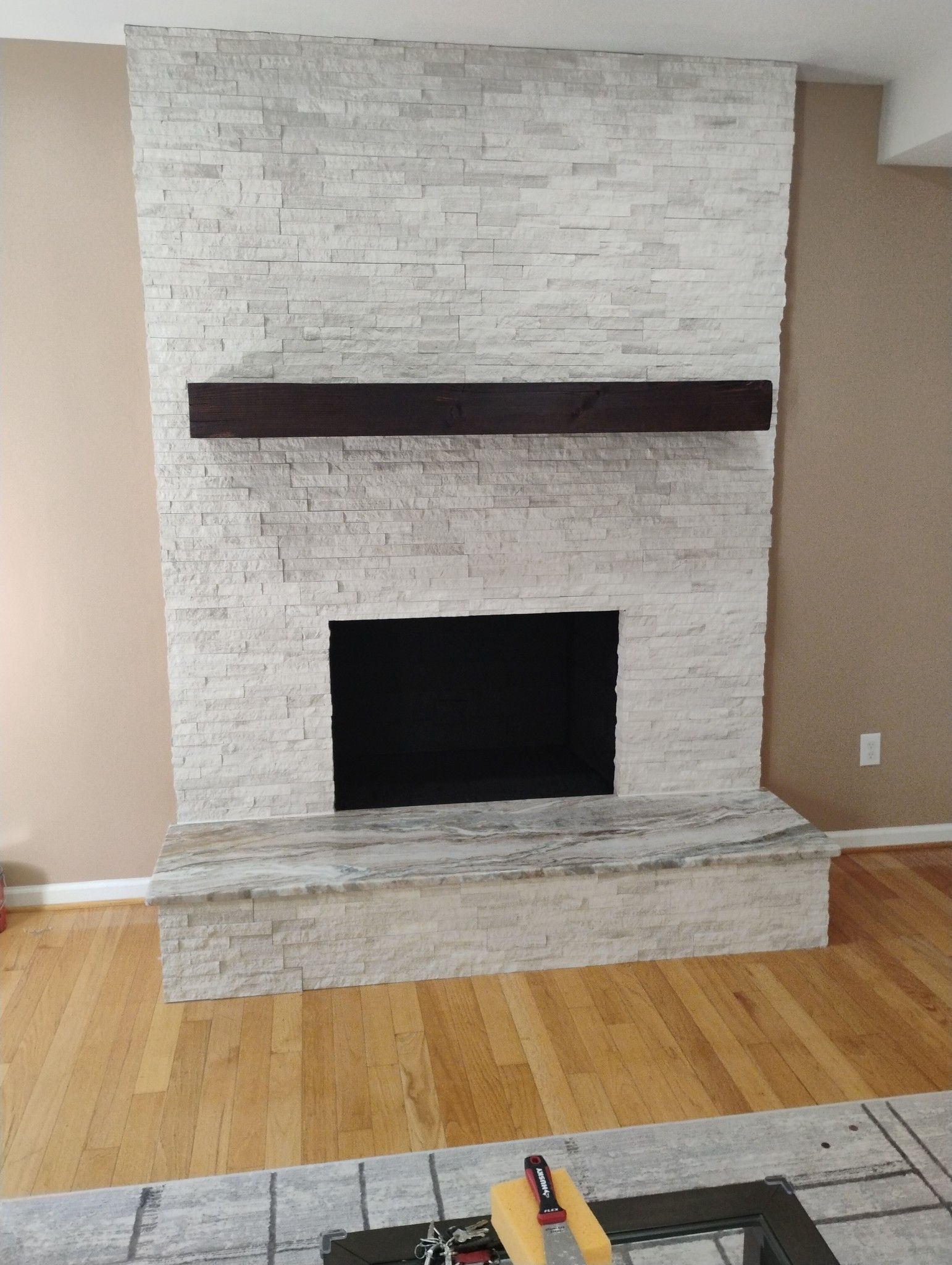 Fireplace with light stone facing, dark wood mantel, and black firebox. Light wood floor.