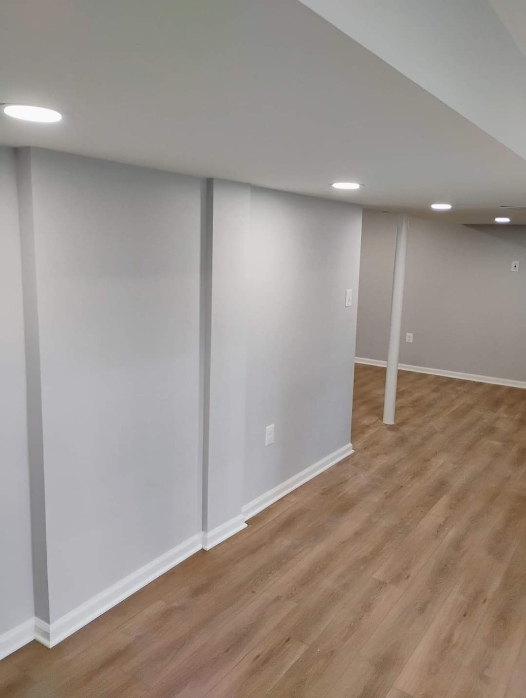 Gray-painted basement walls, white ceiling, and wood-look flooring with recessed lighting.