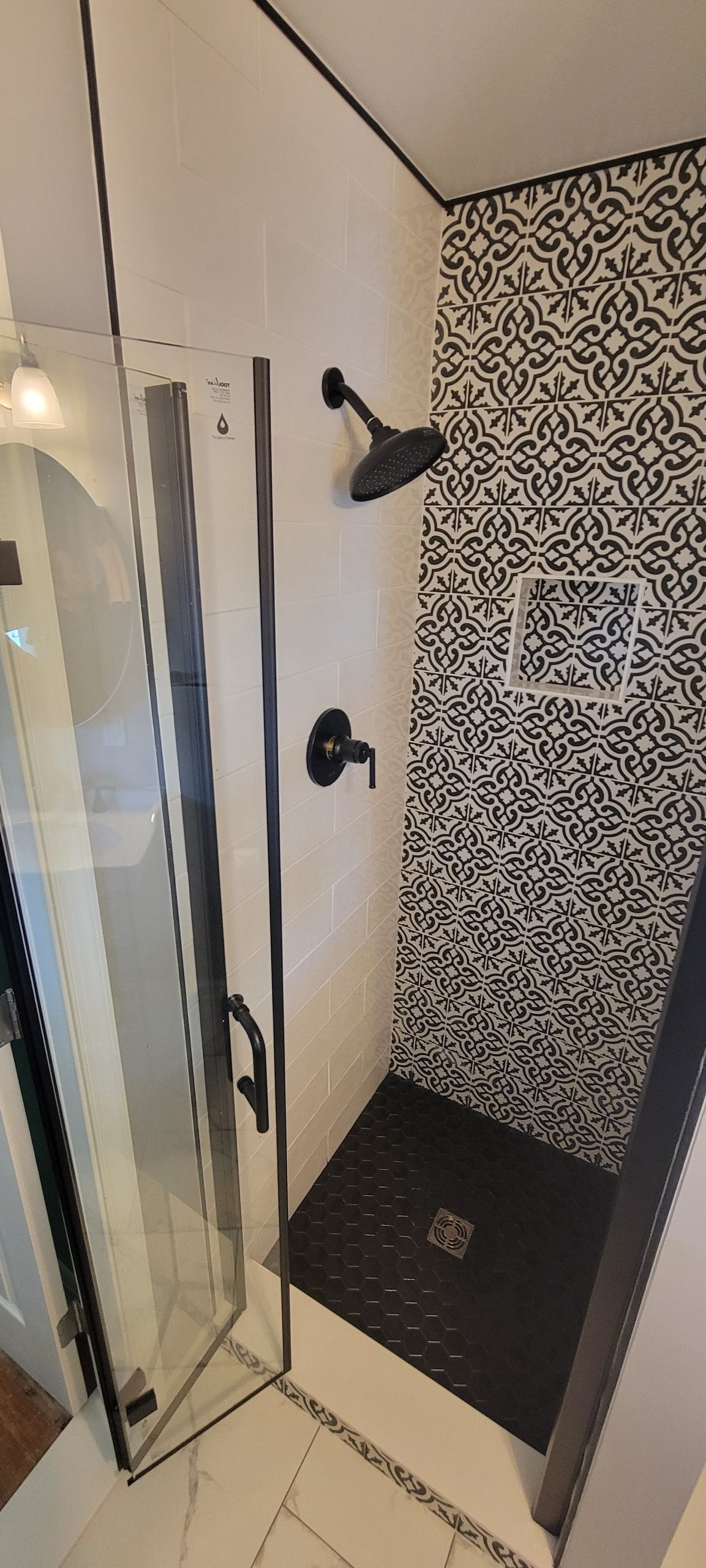 Shower with black fixtures and patterned tile wall.